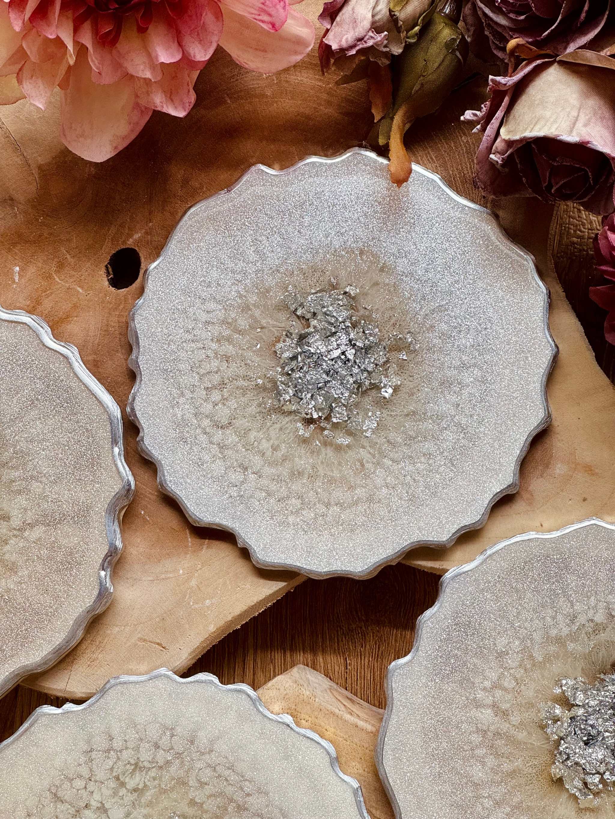 4 zeitlose Untersetzer aus weißem Resin mit silbernen Details auf Holztisch mit Blütenarrangement
