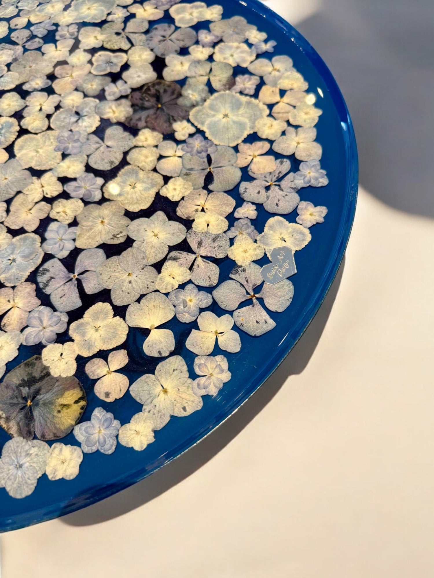 Epoxidharz Couchtisch mit floraler Oberfläche – echte blaue Hortensienblüten im Harz, stilvoll arrangiert auf schwarzem Metallfuß