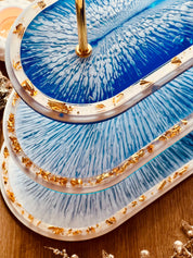 Handgemachte ovale Resin Etagere in Blau-Weiß mit goldenen Akzenten, passend kombinierbar mit einem Tablett, stilvoll und einzigartig.Epoxidharz Etagere Kuchenstaender Blauschimmer mit Blattgold Highlights