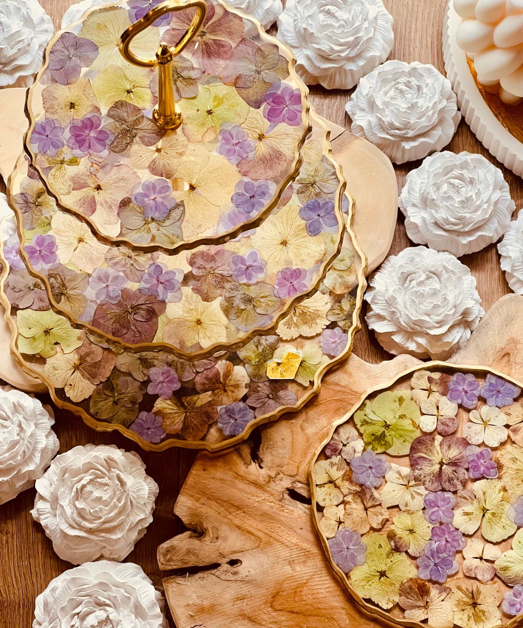 Exklusive Tischdekoration: Etagere aus Resin mit natürlichen und violetten Hortensienblüten und eleganten goldenen Akzenten.