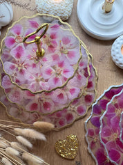 Epoxidharz Etagere aus Resin mit pinken und rosa Blüten auf Holzoberfläche, goldene Details, dekorative Präsentation.
