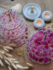 Epoxidharz Etagere aus Resin mit pinken und rosa Blüten, goldenen und silbernen Details, auf Holztisch mit Kerzen.