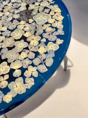 Floraler Epoxidharz Couchtisch mit transparentem Finish und blauen Blüten – rundes Format auf mattschwarzem Metallfuß