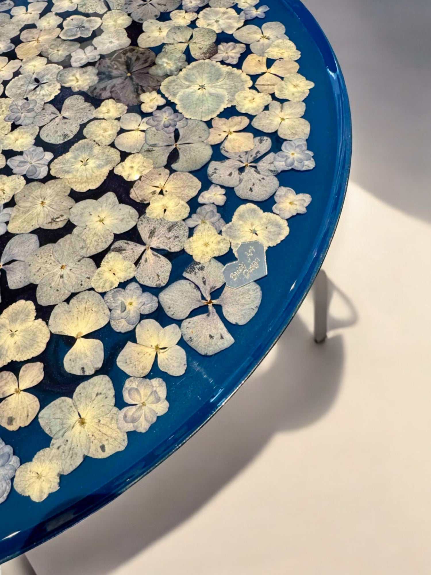 Floraler Epoxidharz Couchtisch mit transparentem Finish und blauen Blüten – rundes Format auf mattschwarzem Metallfuß