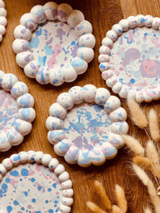 Verspielte Gießkeramik-Untersetzer mit gewelltem Rand und pastellfarbenen Sprenkeln, ideal als dekorativer Schutz für Oberflächen oder als Kerzenhalter.