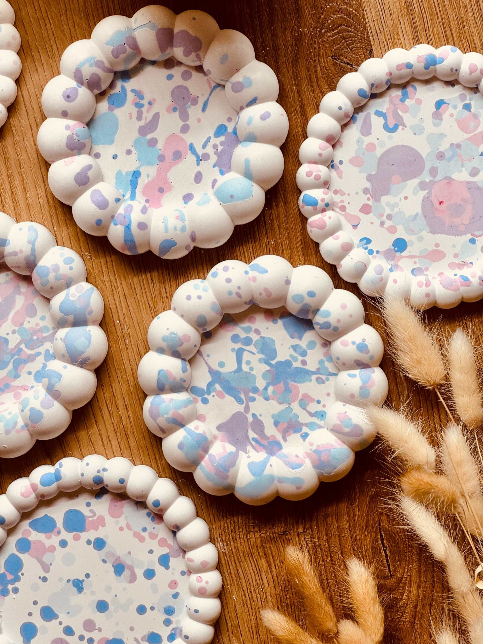 Verspielte Gießkeramik-Untersetzer mit gewelltem Rand und pastellfarbenen Sprenkeln, ideal als dekorativer Schutz für Oberflächen oder als Kerzenhalter.