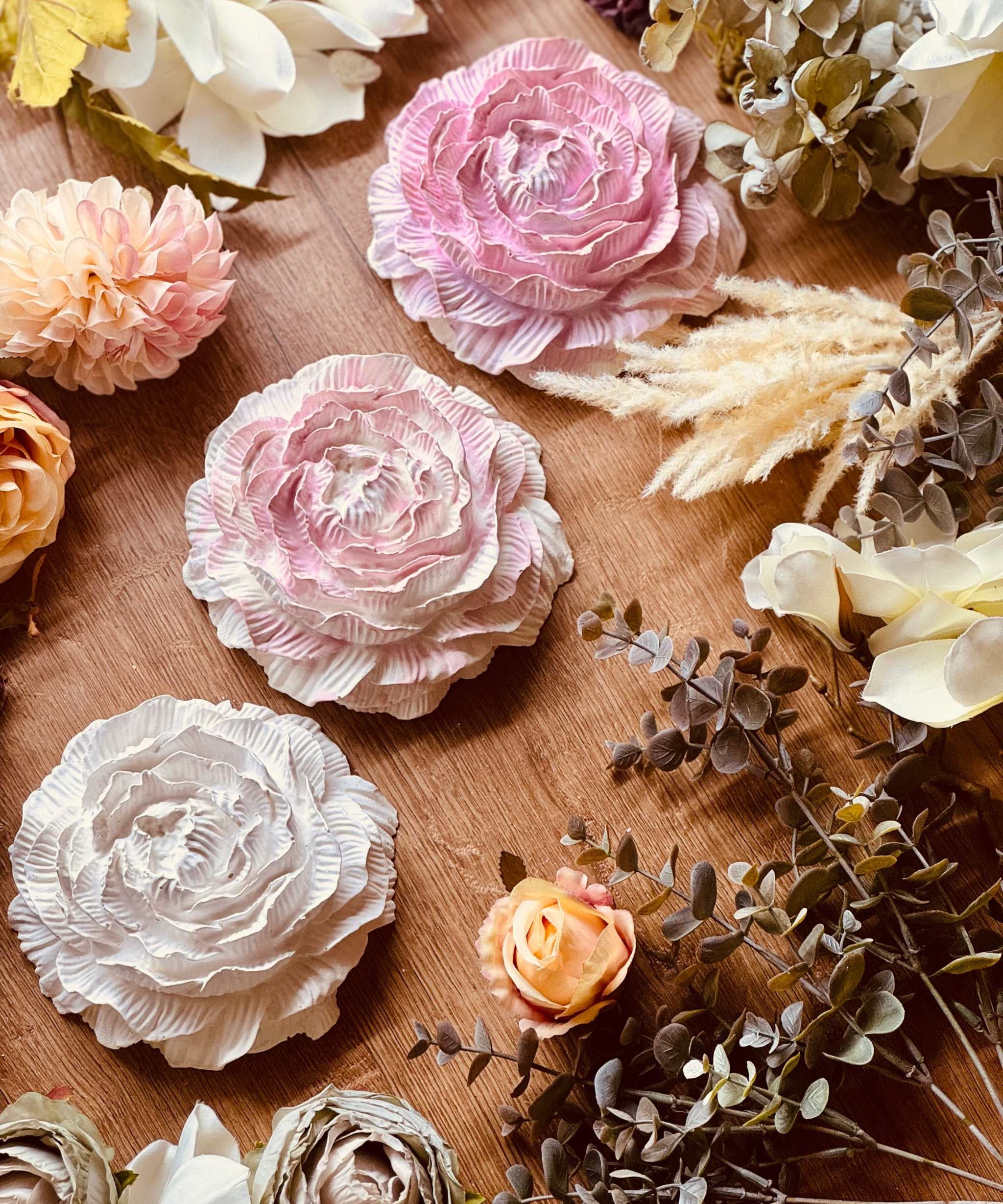 Zart gestaltete Rosenblüten aus Gießkeramik in Rosa, Pink und Creme, dekorativ mit getrockneten Blumen arrangiert, ideale Geschenkidee für Liebhaber floraler Dekoration