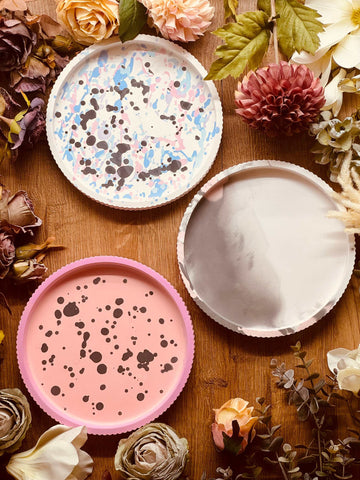 Drei handgefertigte Gießkeramik Tabletts mit einzigartigen Mustern: rosa mit schwarzen Sprenkeln, pastellfarben gesprenkelt, und in dezentem Marmor-Grau. Perfekt als Dekoration oder Serviertablett.Giesskeramik Weisse Deko Tablett buntes Design modern