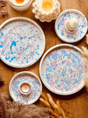 Set aus Gießkeramik-Tabletts in verschiedenen Größen mit pastellfarbenem Sprenkel-Design in Rosa, Blau und Flieder, kombiniert mit handgefertigten Kerzenhaltern, ideal für eine stilvolle Tischdekoration.