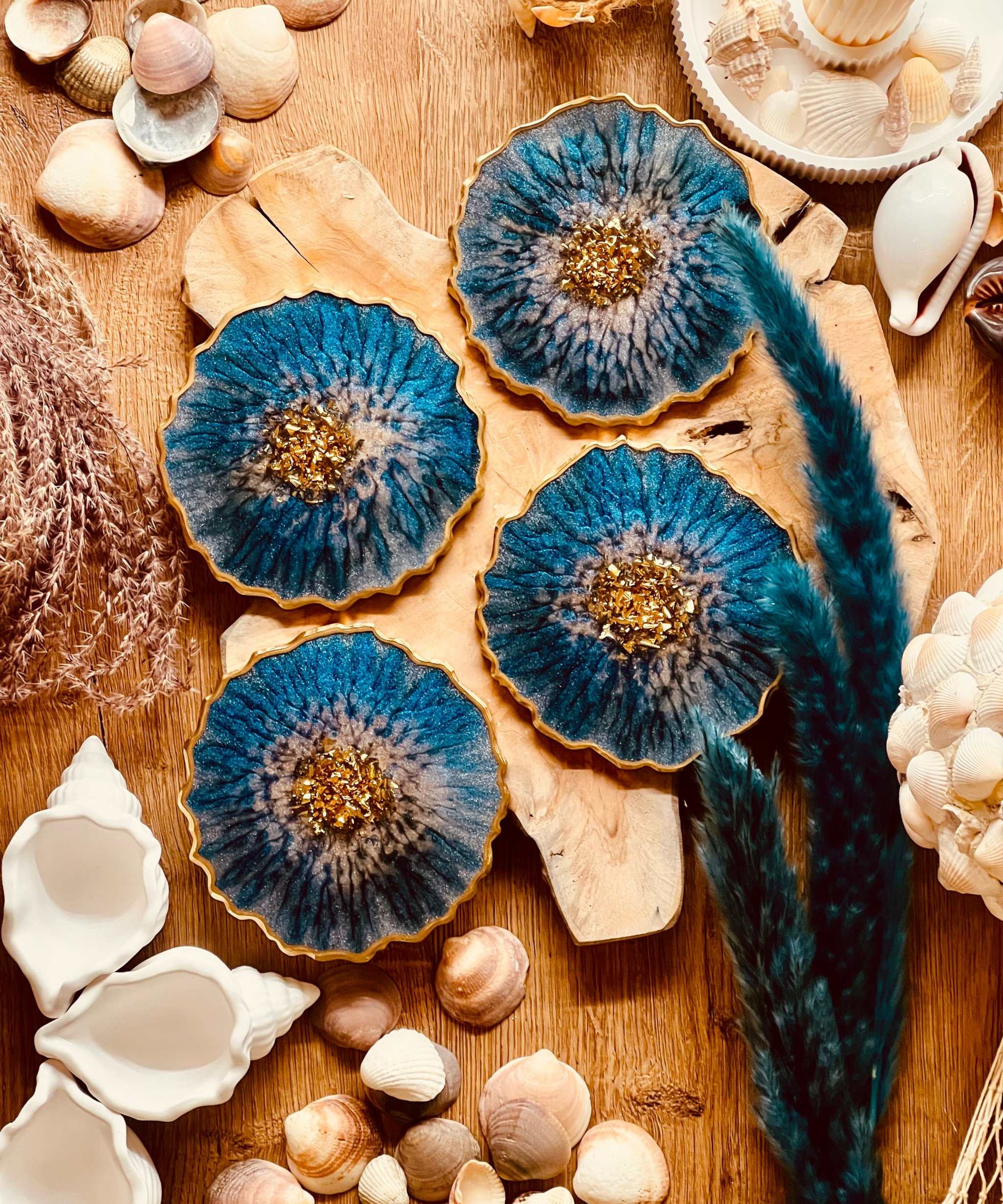 4 Untersetzer aus Resin in Blau mit goldenen Details auf Holztisch mit Muscheln dekoriert