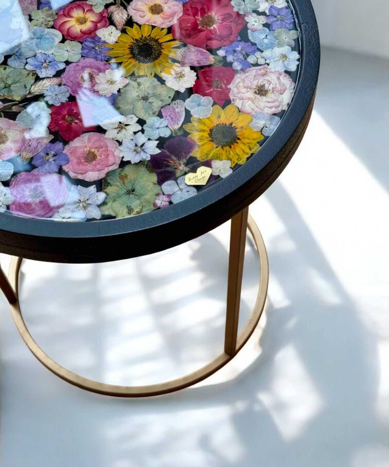 Runder Epoxidharz Couchtisch mit echten getrockneten Blumen und schwarzem Holzrahmen – edles Designstück mit farbenfrohem Blumenmuster und goldfarbenem Metallgestell. Brautstrauß konservieren -  Auch mit deinem Brautstrauß zur Brautstrauss Konservierung