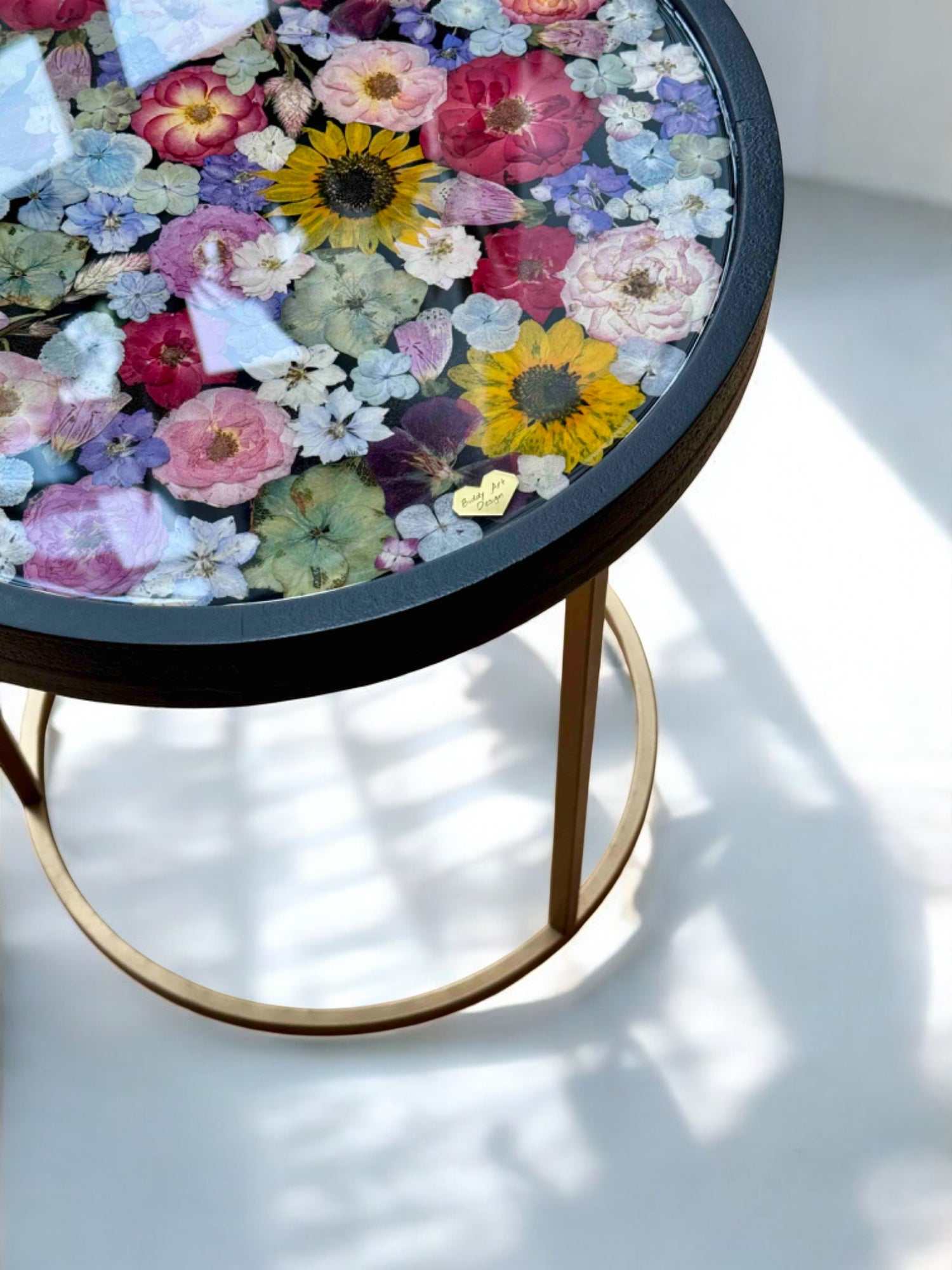 Runder Epoxidharz Couchtisch mit echten getrockneten Blumen und schwarzem Holzrahmen – edles Designstück mit farbenfrohem Blumenmuster und goldfarbenem Metallgestell