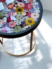 Runder Epoxidharz Couchtisch mit echten getrockneten Blumen und schwarzem Holzrahmen – edles Designstück mit farbenfrohem Blumenmuster und goldfarbenem Metallgestell. Brautstrauß konservieren -  Auch mit deinem Brautstrauß zur Brautstrauss Konservierung
