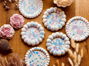 Runde Gießkeramik-Untersetzer mit aufgeblasenem Rand und Spritzmuster in zarten Pastelltönen, handgefertigt und einzeln erhältlich, perfekt für Getränke und Kerzen.
