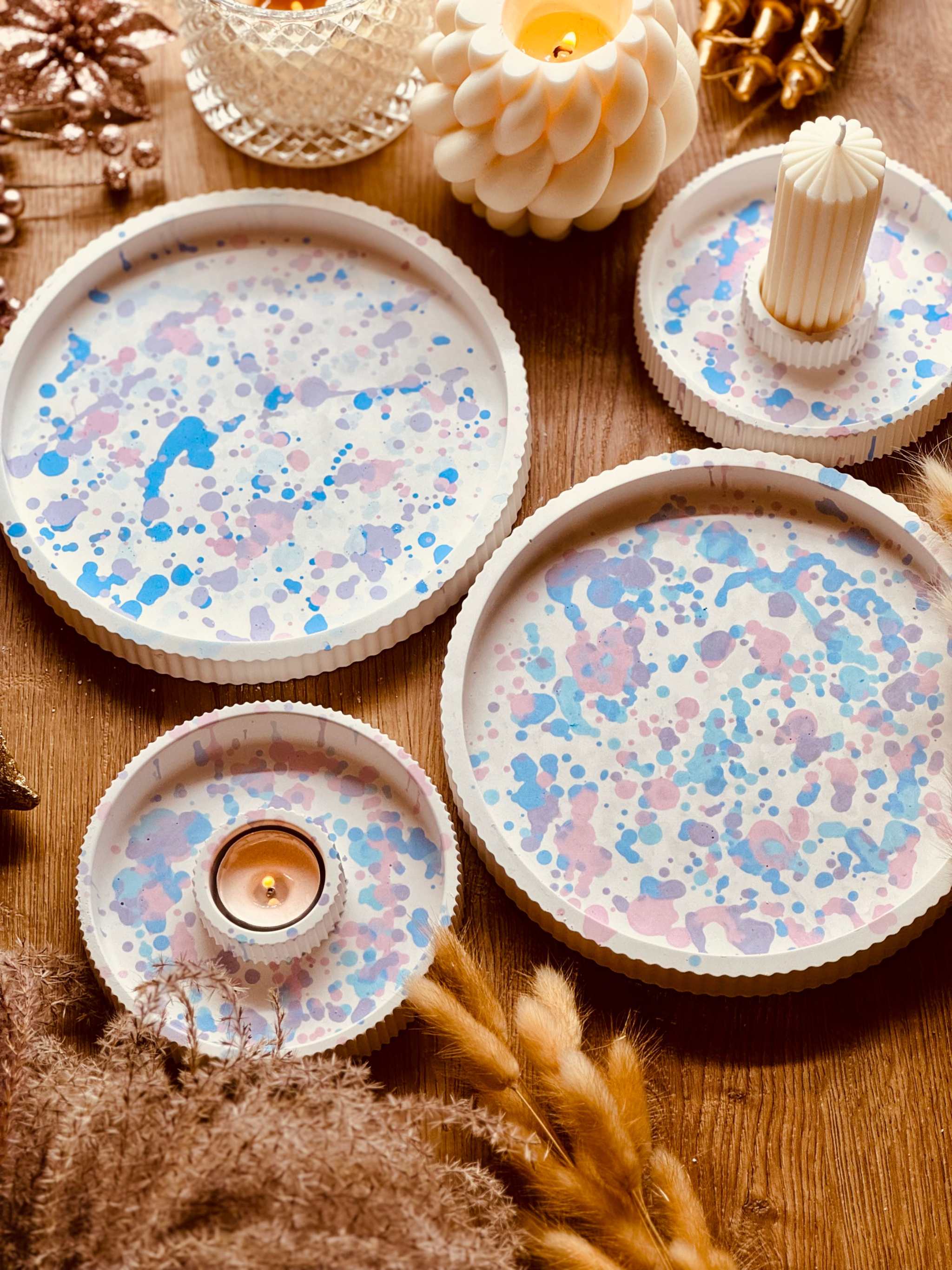 Runde Tabletts aus Gießkeramik mit buntem Pastellmuster und passenden Kerzenhaltern, ideal für elegante Tischarrangements oder als stilvolle Wohnaccessoires.