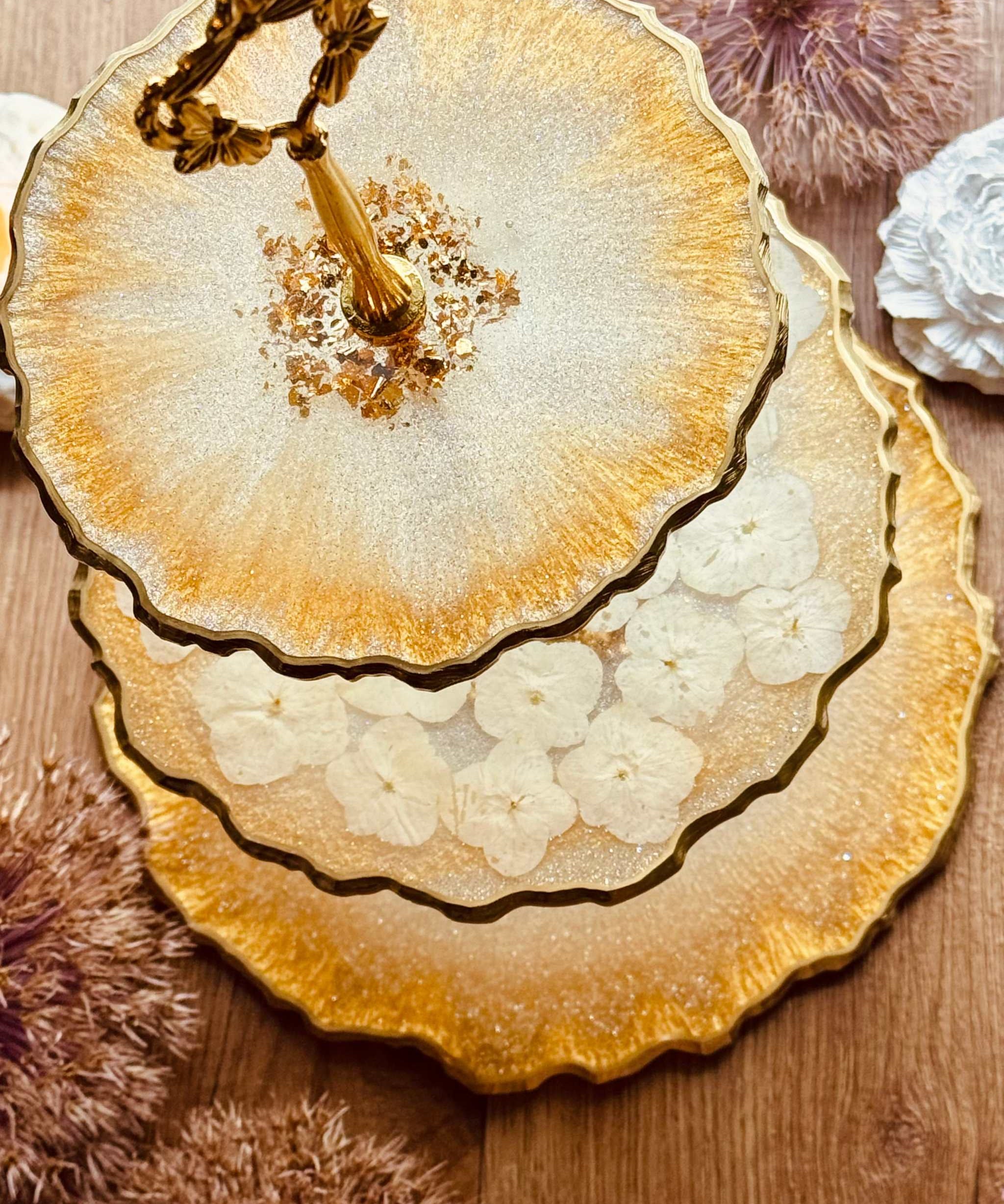 dreistöckige goldene Epoxidharz Etagere mit weißen Hortensien, eleganter Kuchenständer und Deko, handgefertigt und stilvoll