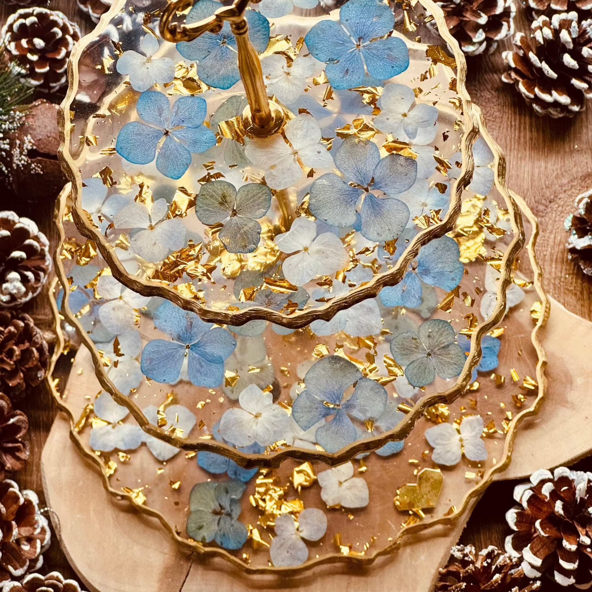 Elegante 3-stöckige Epoxidharz Etagere mit goldenen Akzenten und blauen Hortensien, handgefertigt und ideal für festliche Tischdekorationen.