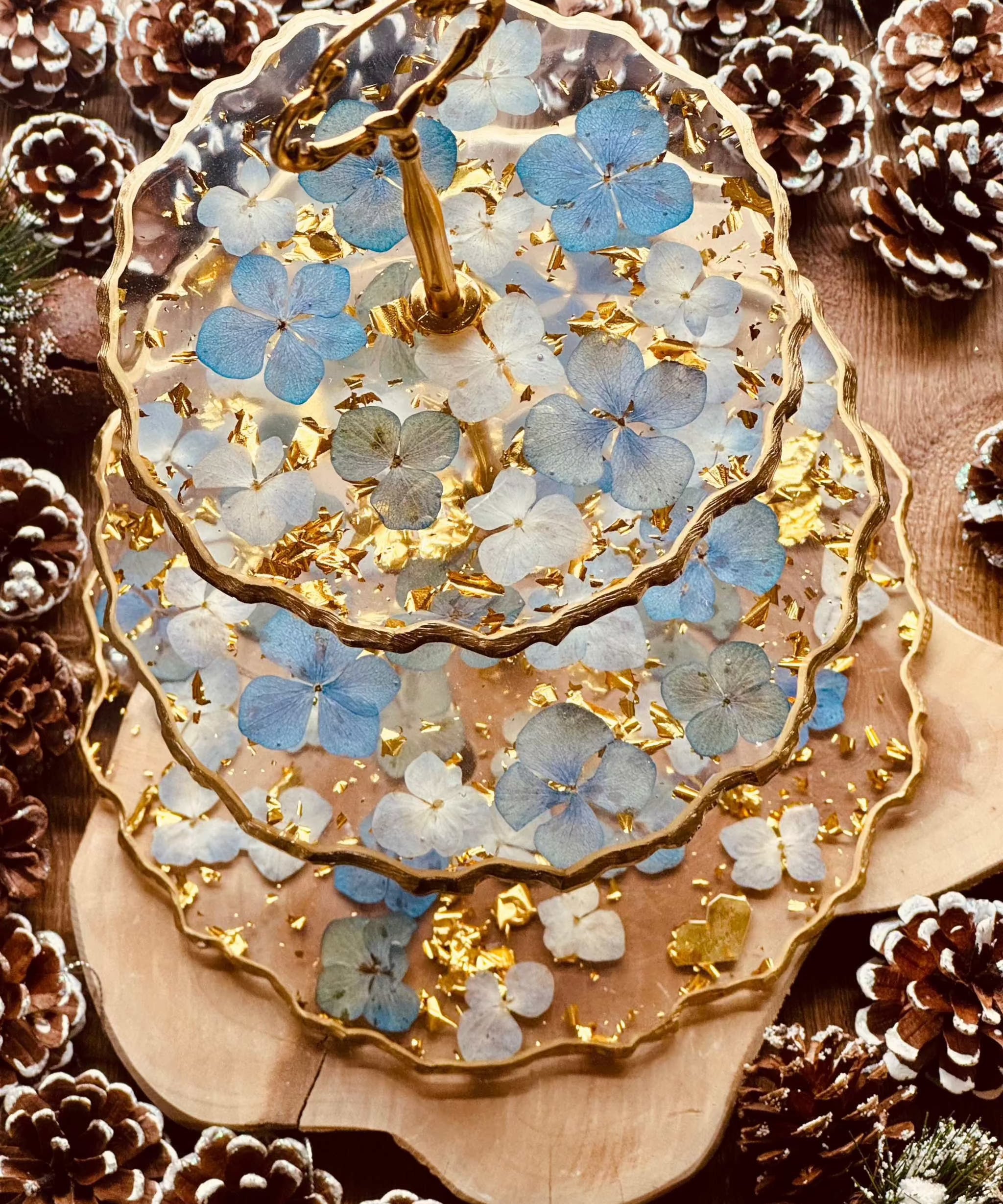 Elegante 3-stöckige Epoxidharz Etagere mit goldenen Akzenten und blauen Hortensien, handgefertigt und ideal für festliche Tischdekorationen.