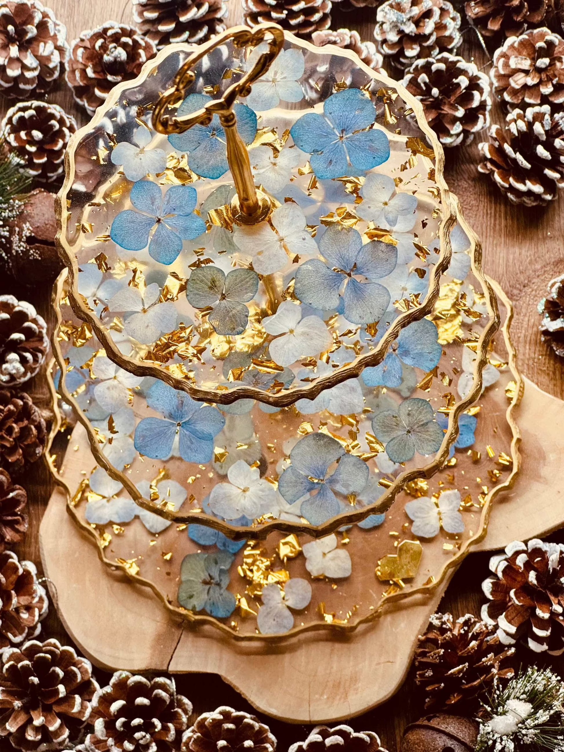 Elegante 3-stöckige Epoxidharz Etagere mit goldenen Akzenten und blauen Hortensien, handgefertigt und ideal für festliche Tischdekorationen.