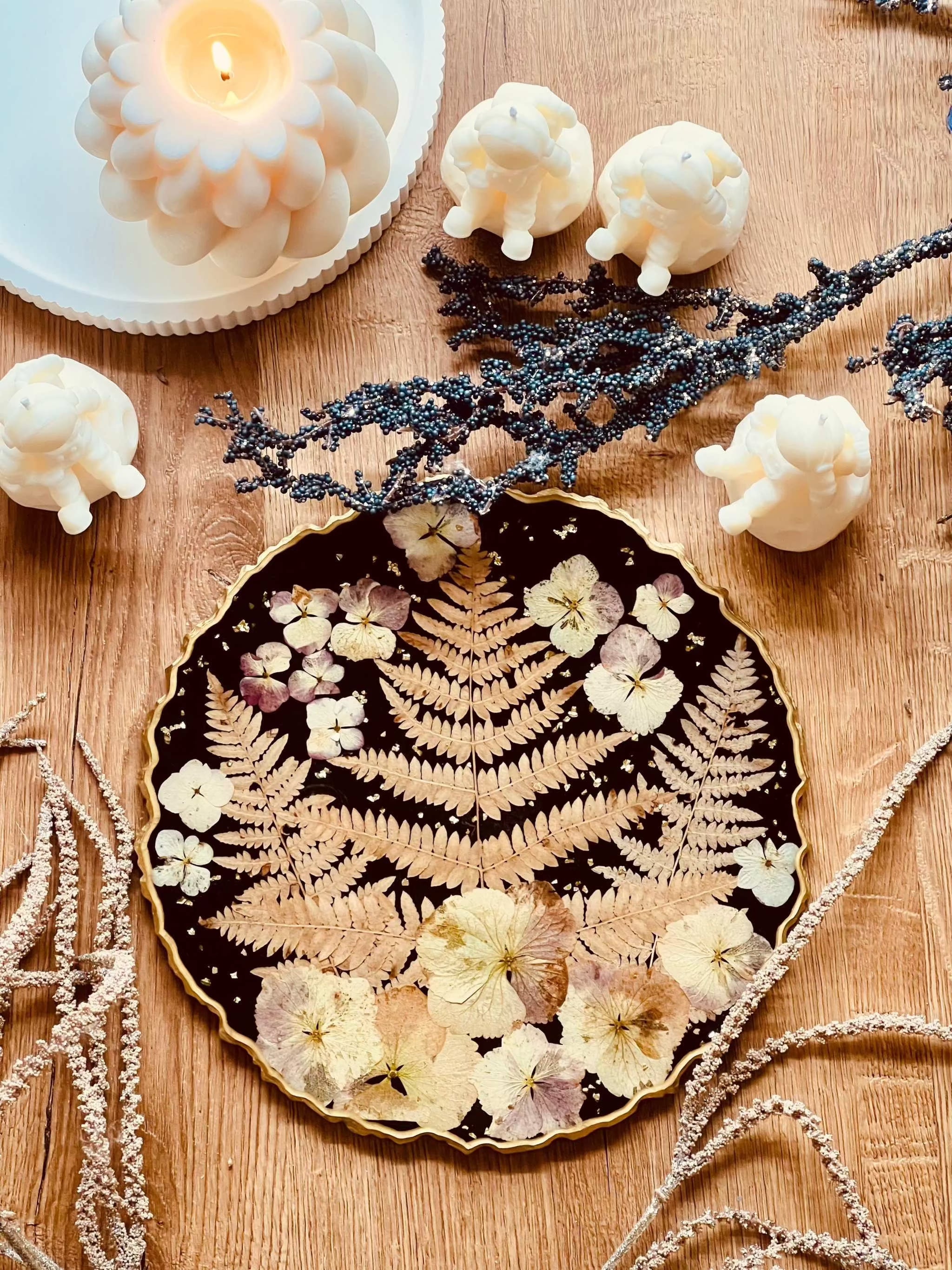 Schwarzes handgemachtes Tablett aus Resin mit getrockneten Blumen und goldenen Details auf Holztisch