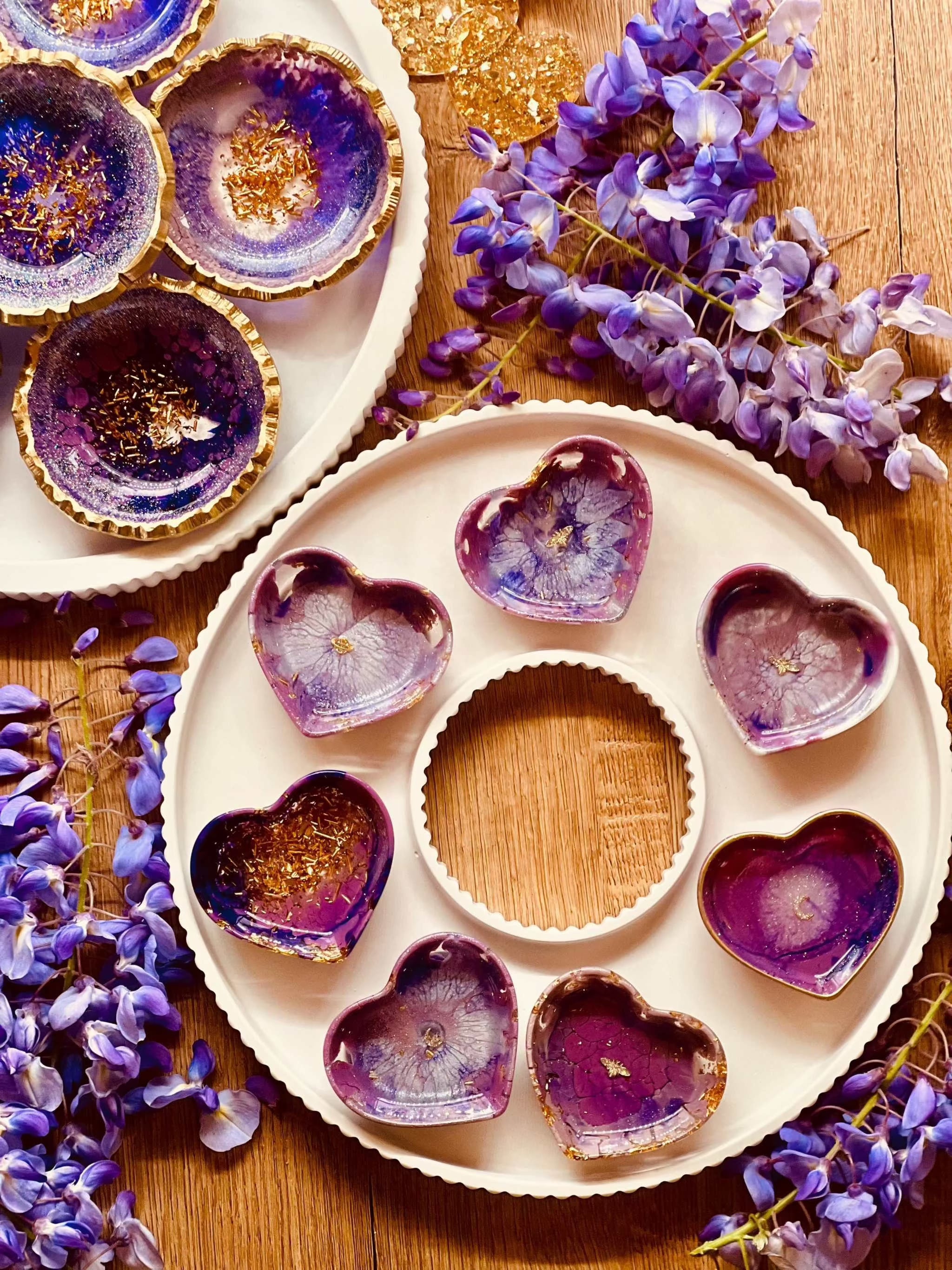 Handgemachte lila Schmuckschalen aus Resin mit goldenen Details in Herzform als Unikat auf Holz mit blauer Blüten-Dekoration