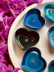 Handgemalte Schmuckschalen aus Resin in Herzform mit silbernen Details auf weißem Teller, umgeben von rosa Blumen