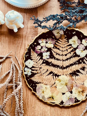 Schwarzes handgemachtes Tablett aus Resin mit getrockneten Blumen und goldenen Details auf Holztisch