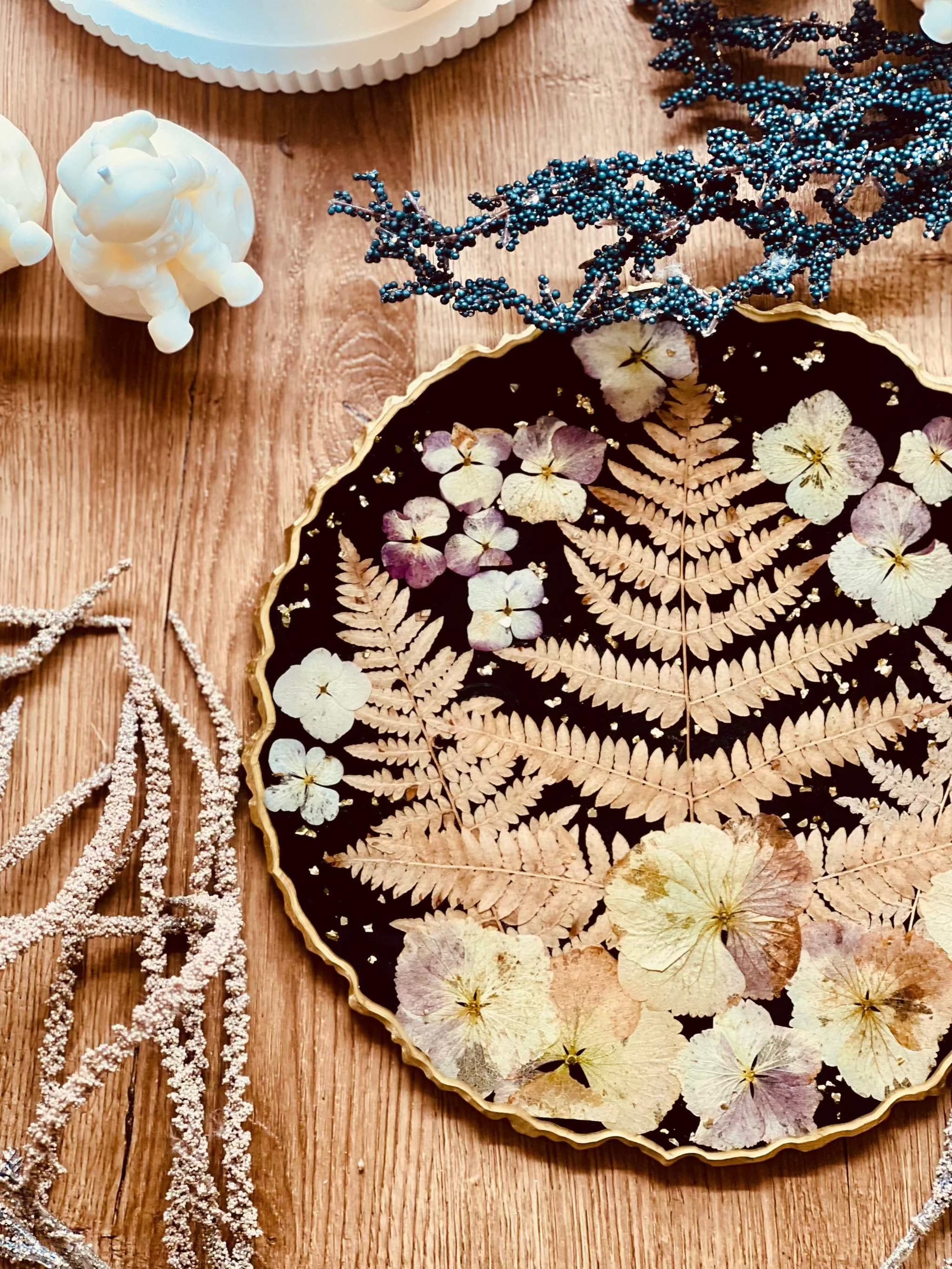 Schwarzes handgemachtes Tablett aus Resin mit getrockneten Blumen und goldenen Details auf Holztisch