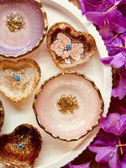 handgemachte schmuckschalen aus resin in beerentönen mit goldenen details in herzform und rund auf weißem teller mit lila blumen