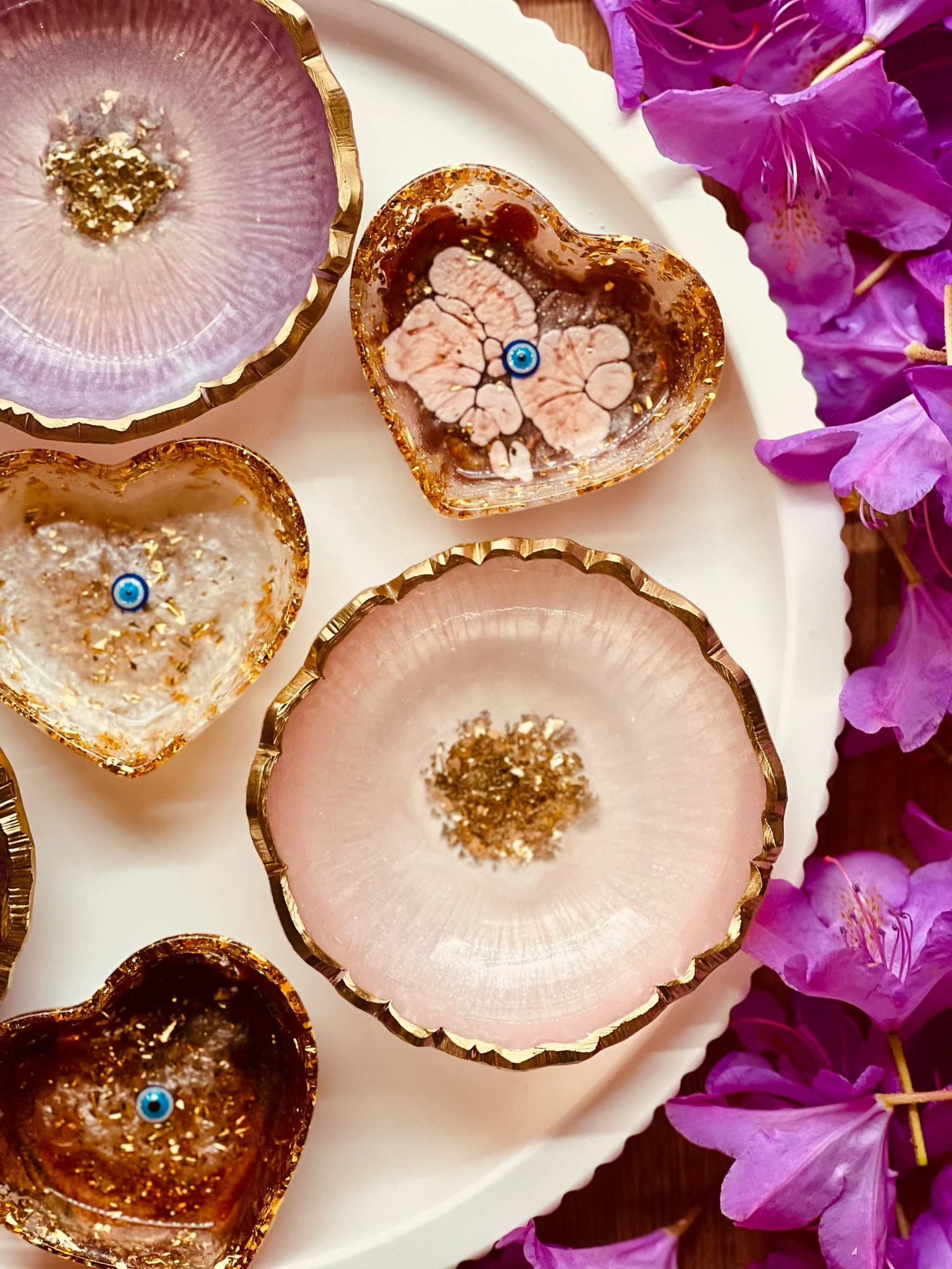 handgemachte schmuckschalen aus resin in beerentönen mit goldenen details in herzform und rund auf weißem teller mit lila blumen
