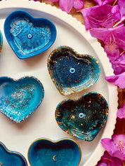 Handgemachte Herzförmige Schmuckschalen aus Resin in verschiedenen Blautönen mit silbernen Details auf weißem Teller mit rosa Blumen