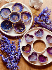 Handgemachte lila Schmuckschalen aus Resin mit goldenen Details in Herz- und Rundform auf weißem Tablett dekoriert