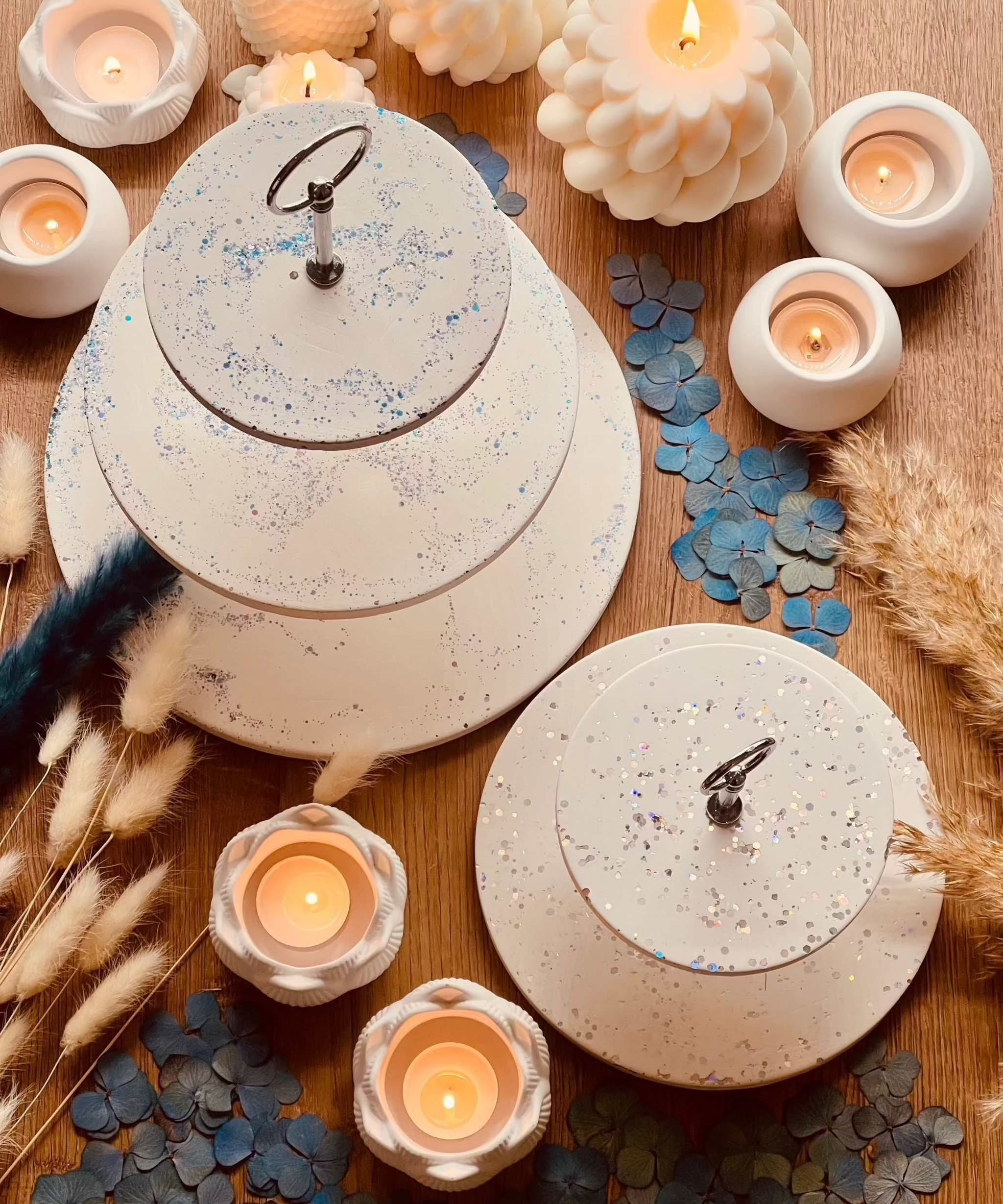 White Gießkeramik tiered stand with sparkling highlights, surrounded by candles and decor in two sizes.Giesskeramik weisse Deko Etagere mit Glanzdetails