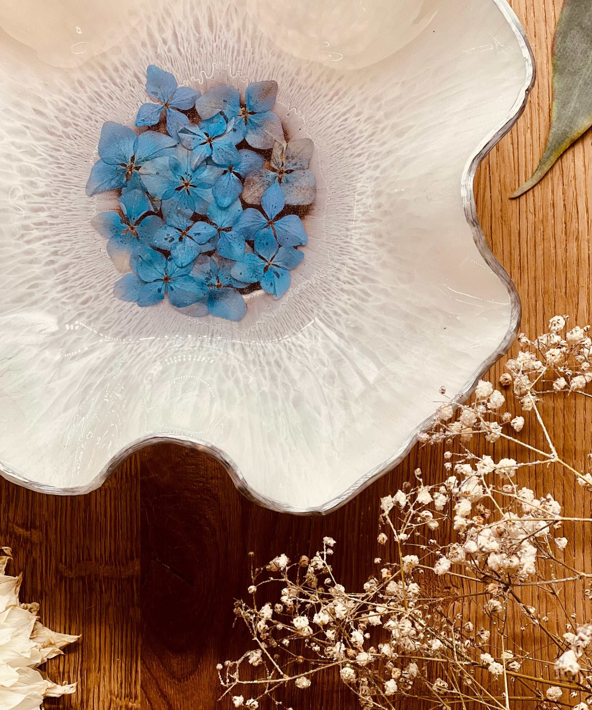 Handgemachte weiße Resin Schale mit silbernen Details und getrockneten blauen Hortensien auf Holztisch
