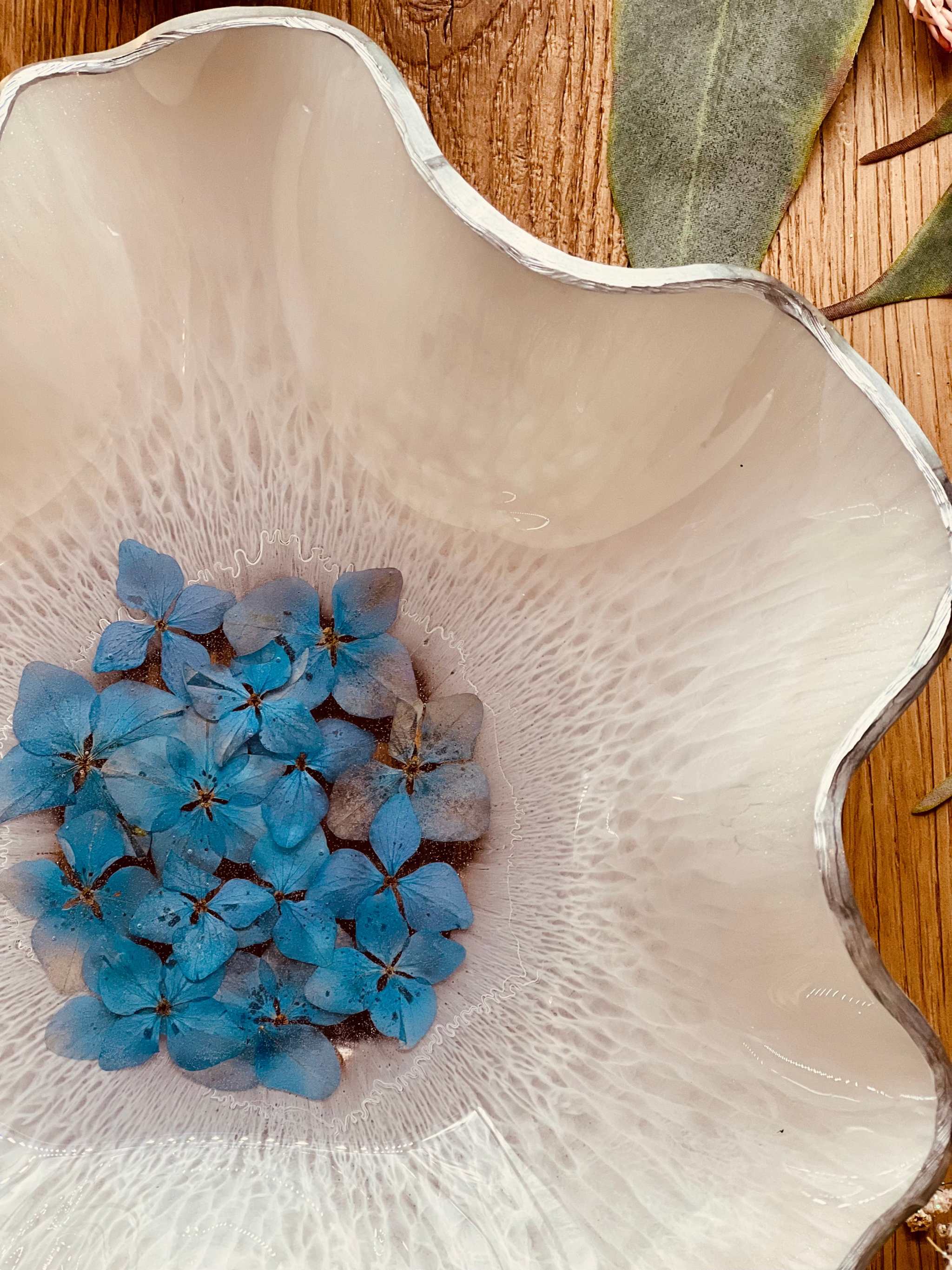 Schale aus Resin in Weiß mit silbernem Rand und handgetrockneten blauen Hortensien dekorativ auf Holztisch