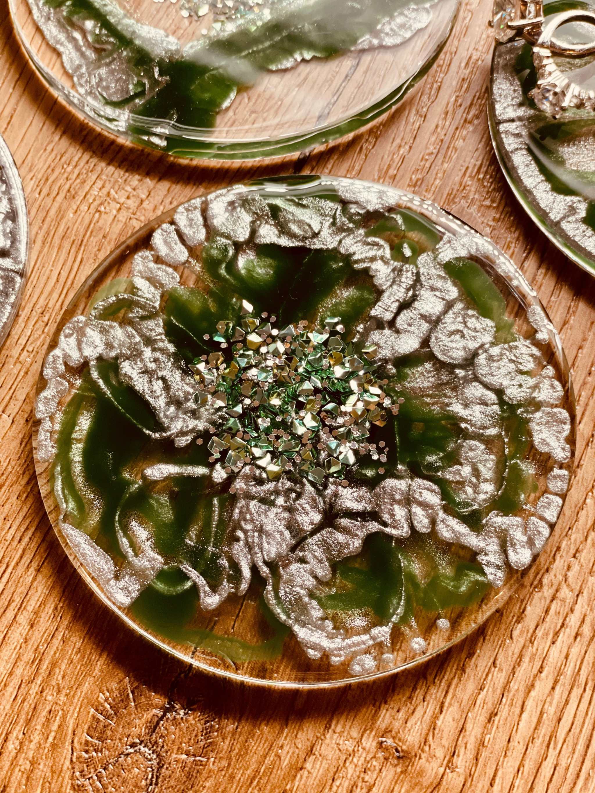 Acht handgemachte runde Resin-Untersetzer in Grün mit silbernen Details auf Holztisch