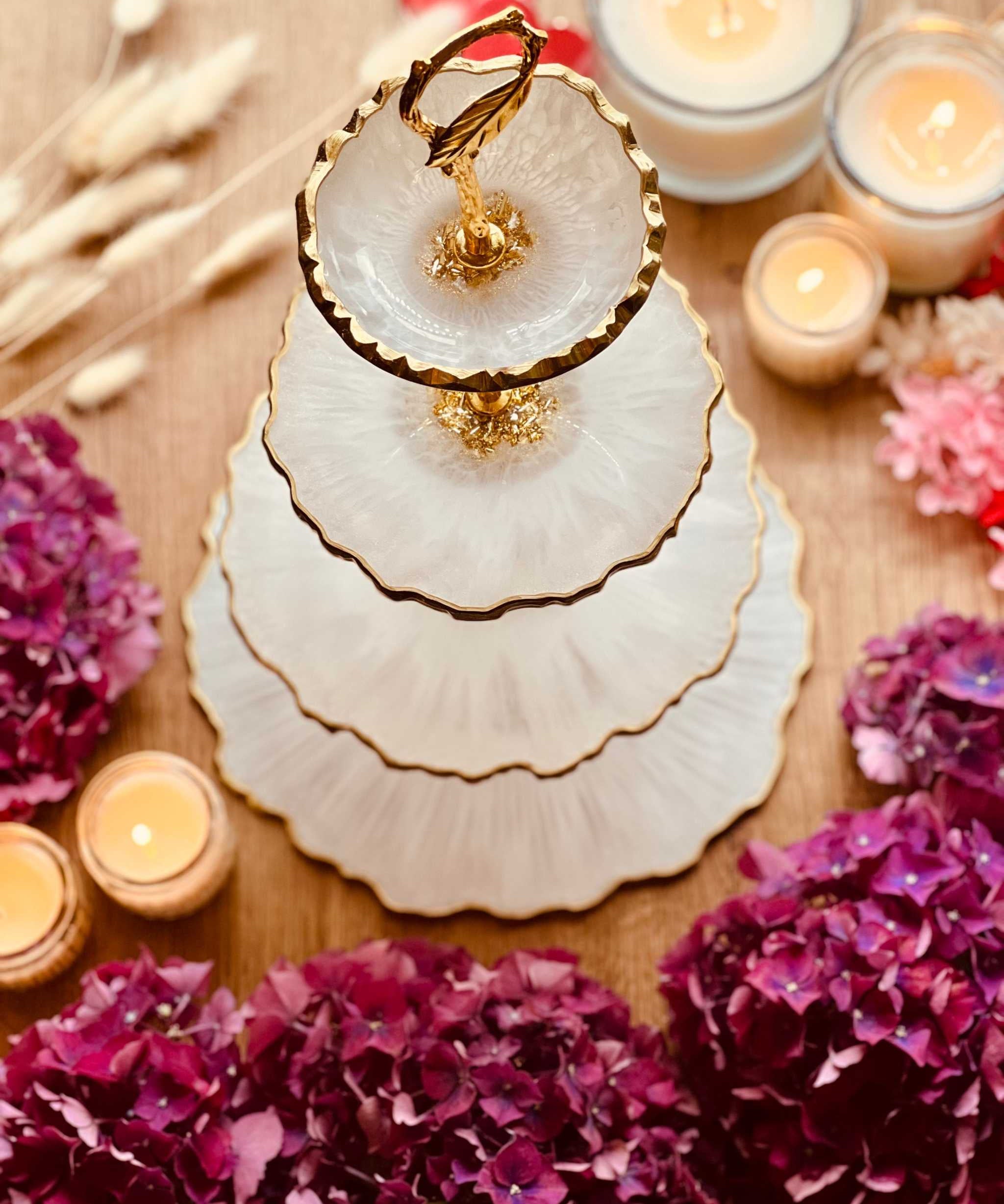 Vierstöckige Etagere aus Resin mit goldenen Rändern, handgemacht und dekorativ auf einem Holztisch mit Kerzen und Blumen