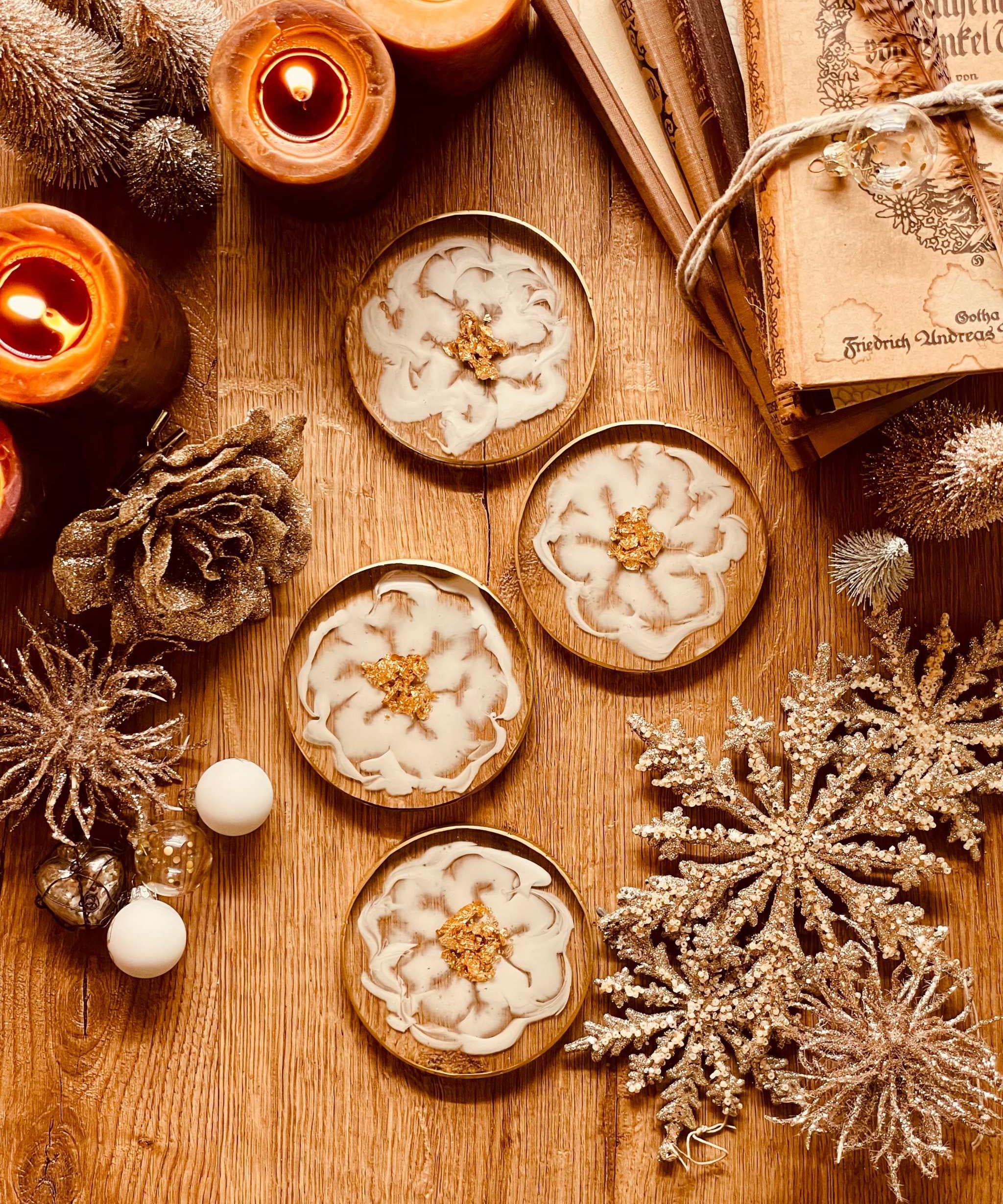 4 exklusive Untersetzer aus weißem Resin mit goldenen Details auf Holzoberfläche neben Kerzen und Weihnachtsdekoration