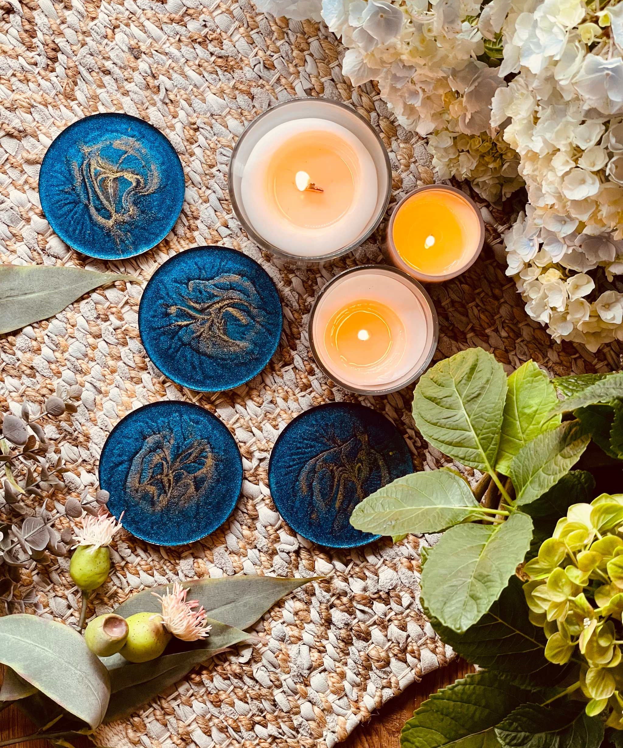 4 handgemachte blaue Resin Untersetzer mit goldenen Details auf natürlichem Tischläufer mit Kerzen und Blumenarrangement