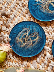 4 Untersetzer aus Resin in Blau mit goldenen Details auf geflochtener Unterlage
