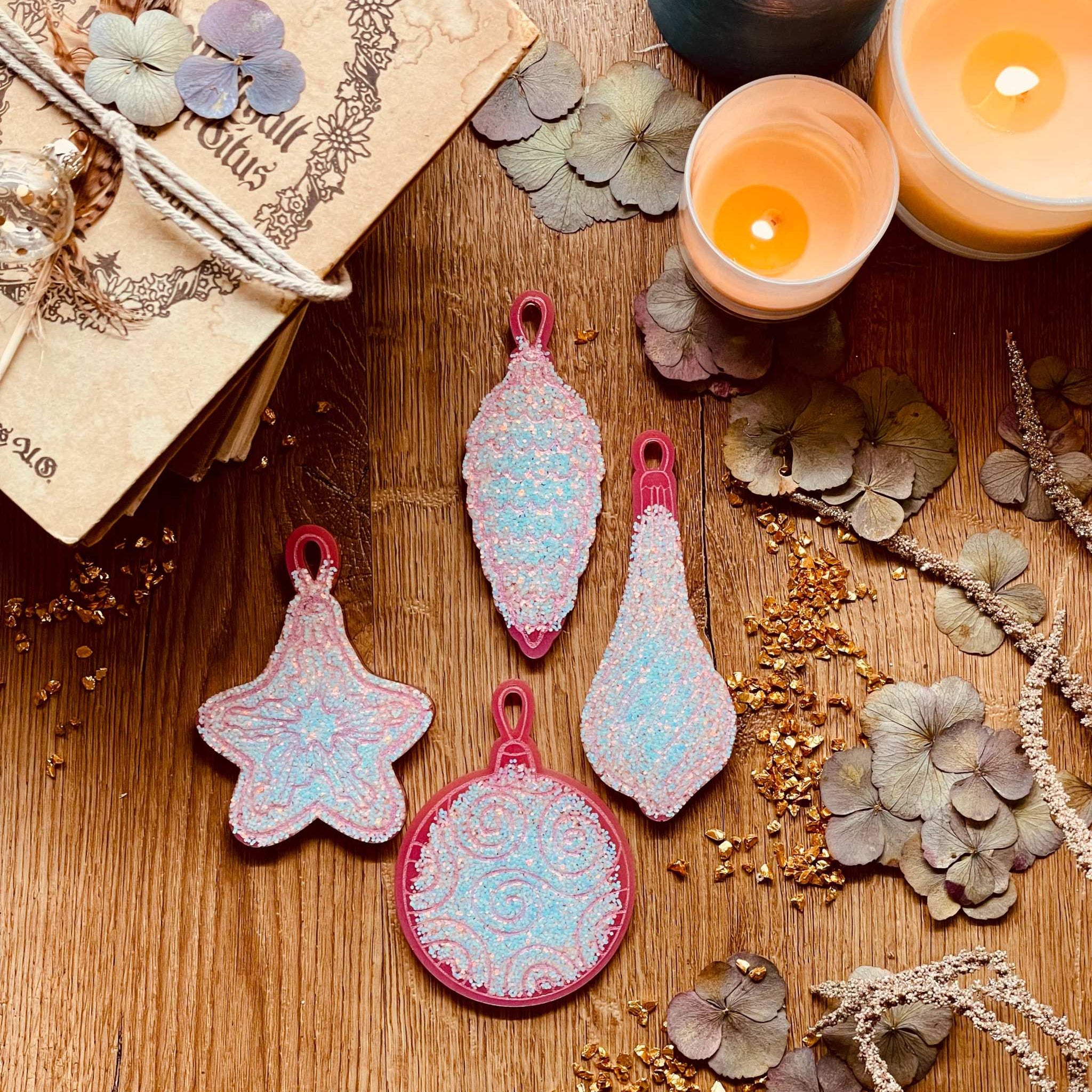Pink and silver resin Christmas tree ornaments set on a wooden surface, featuring four unique handmade pieces.
