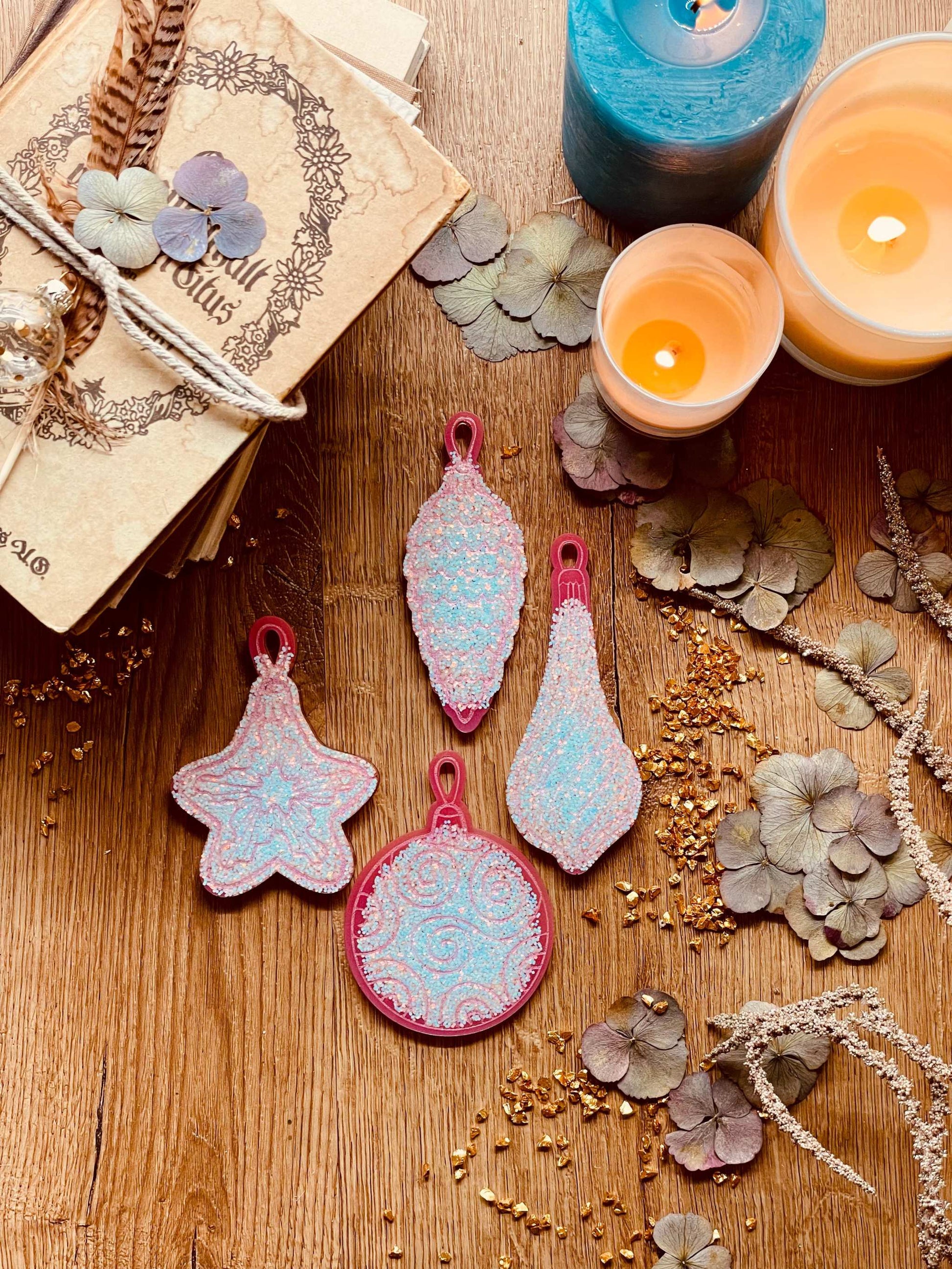 Pink and silver resin Christmas tree ornaments set on a wooden surface, featuring four unique handmade pieces.