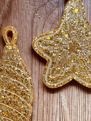 Goldene handgemachte Weihnachtsbaumanhänger aus Resin in Stern- und Tropfenform mit Glitzerdetails auf Holzuntergrund