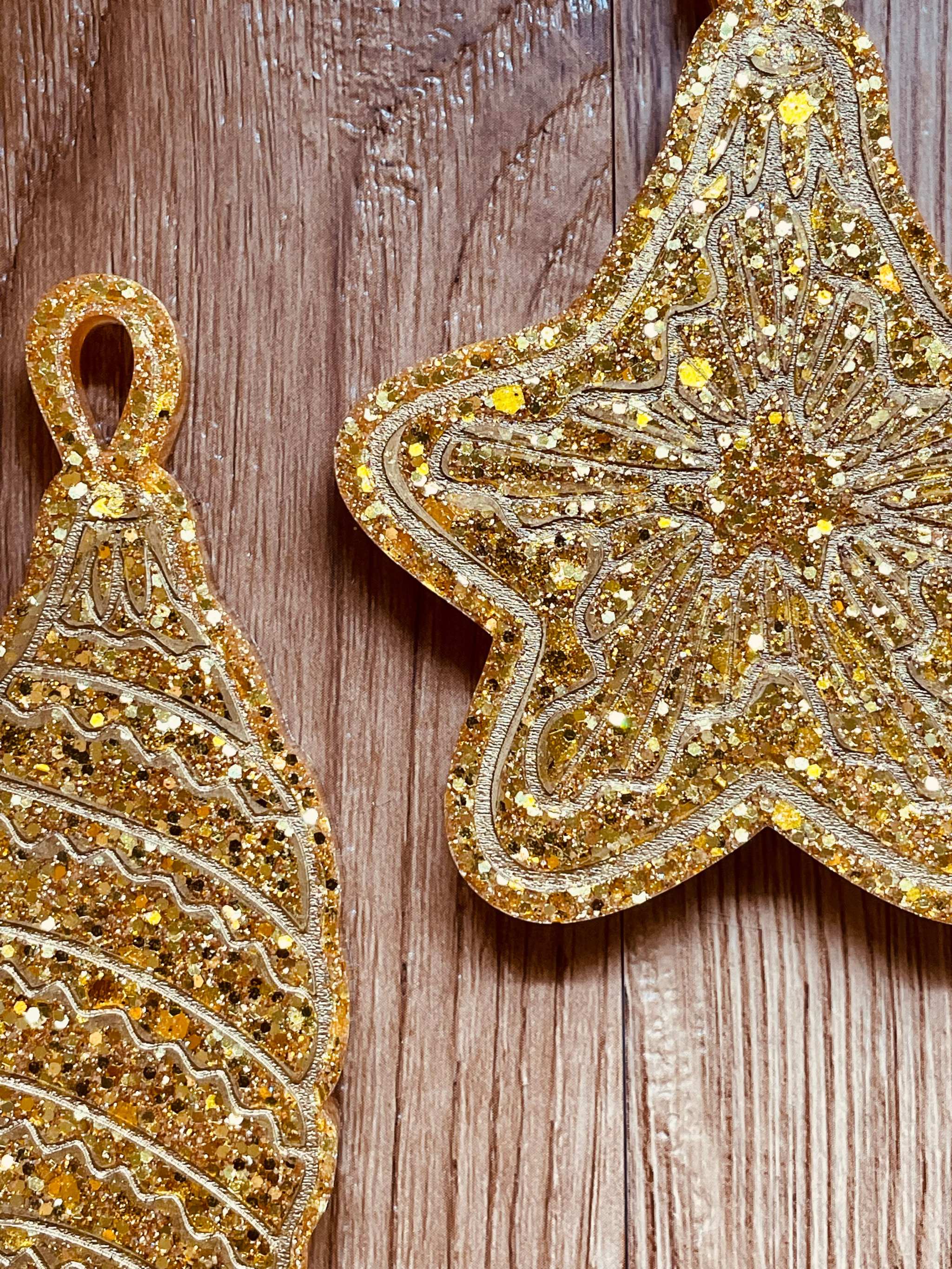 Goldene handgemachte Weihnachtsbaumanhänger aus Resin in Stern- und Tropfenform mit Glitzerdetails auf Holzuntergrund