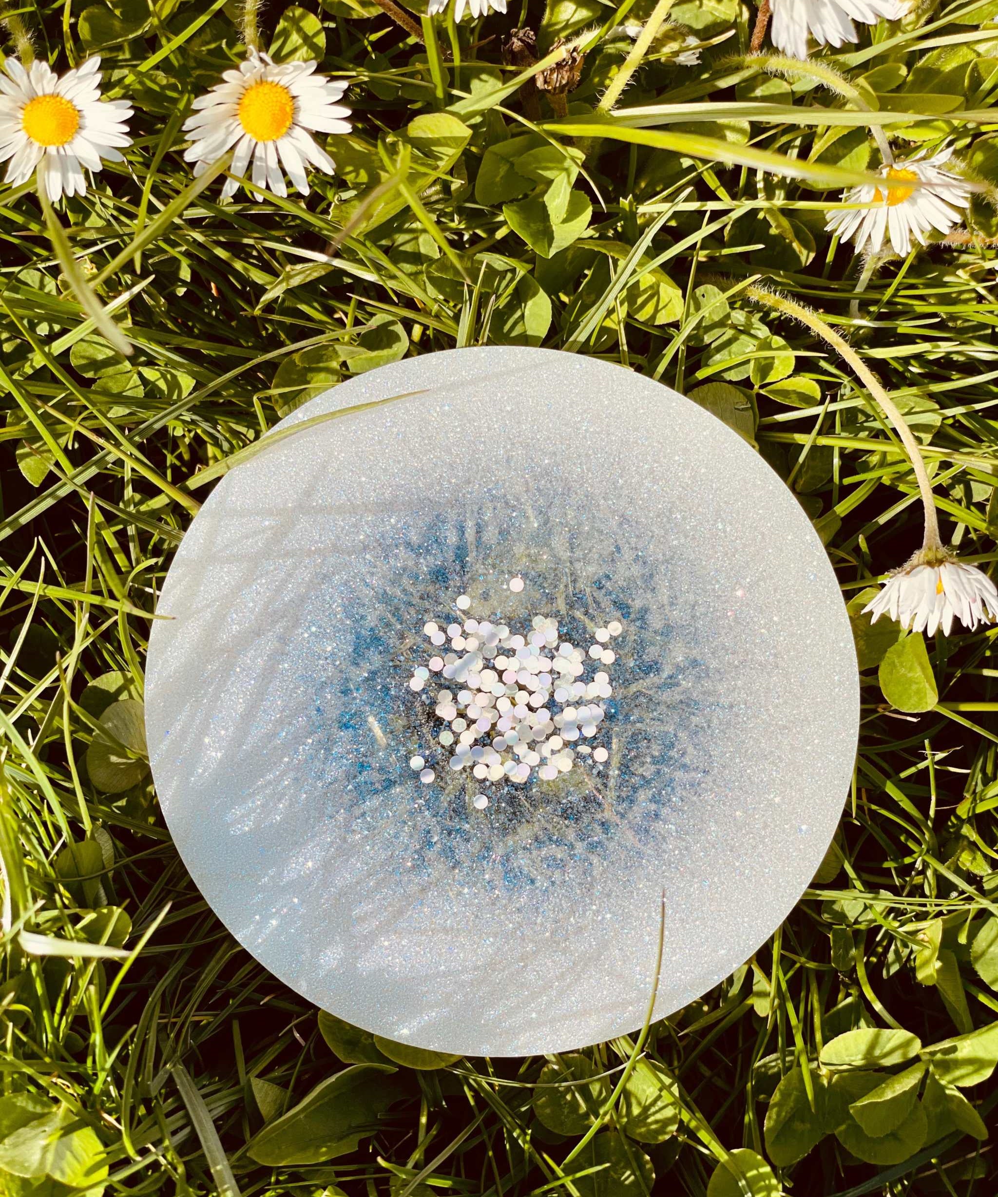 Runder weißer Untersetzer aus Resin mit glitzernden Details auf grüner Wiese