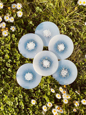 Sechs handgemachte weiße Untersetzer aus Resin mit glitzernden Details auf Wiese mit Blumen