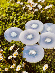 Sechs handgemachte weiße Untersetzer aus Resin mit Glitzer, dekorativ auf Wiese gelegen, Durchmesser ca. 10 cm