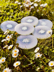 6 handgemachte weiße Untersetzer aus Resin mit glitzernden Details auf Wiese mit Blumen