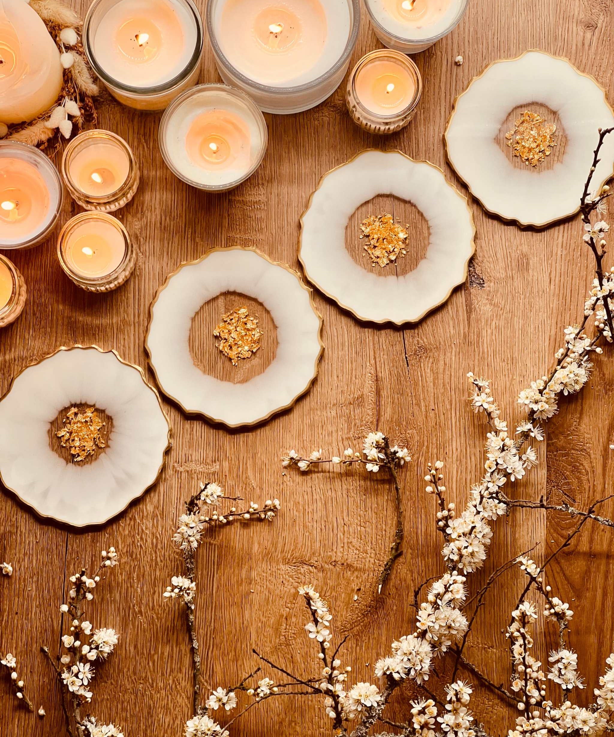 4 glitzernde weiße Resin Untersetzer mit goldenen Details auf Holztisch mit Kerzen und Dekozweigen