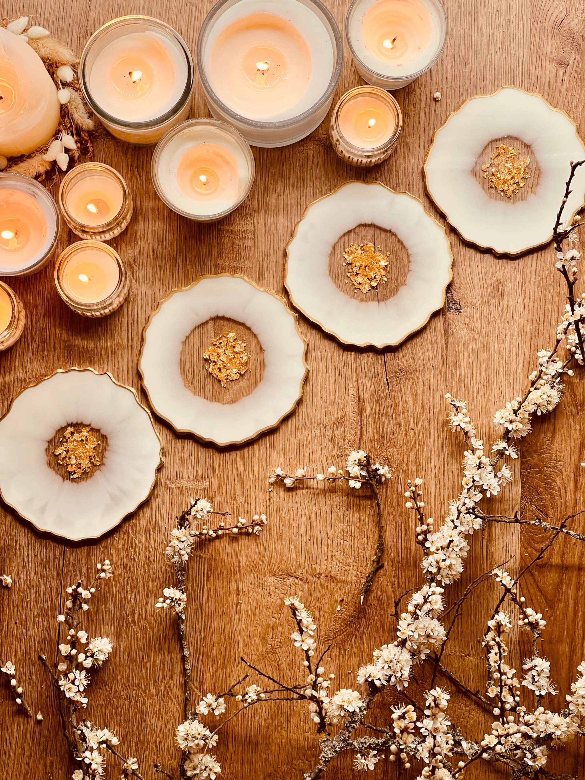 4 glitzernde weiße Resin Untersetzer mit goldenen Details auf Holztisch mit Kerzen und Dekozweigen